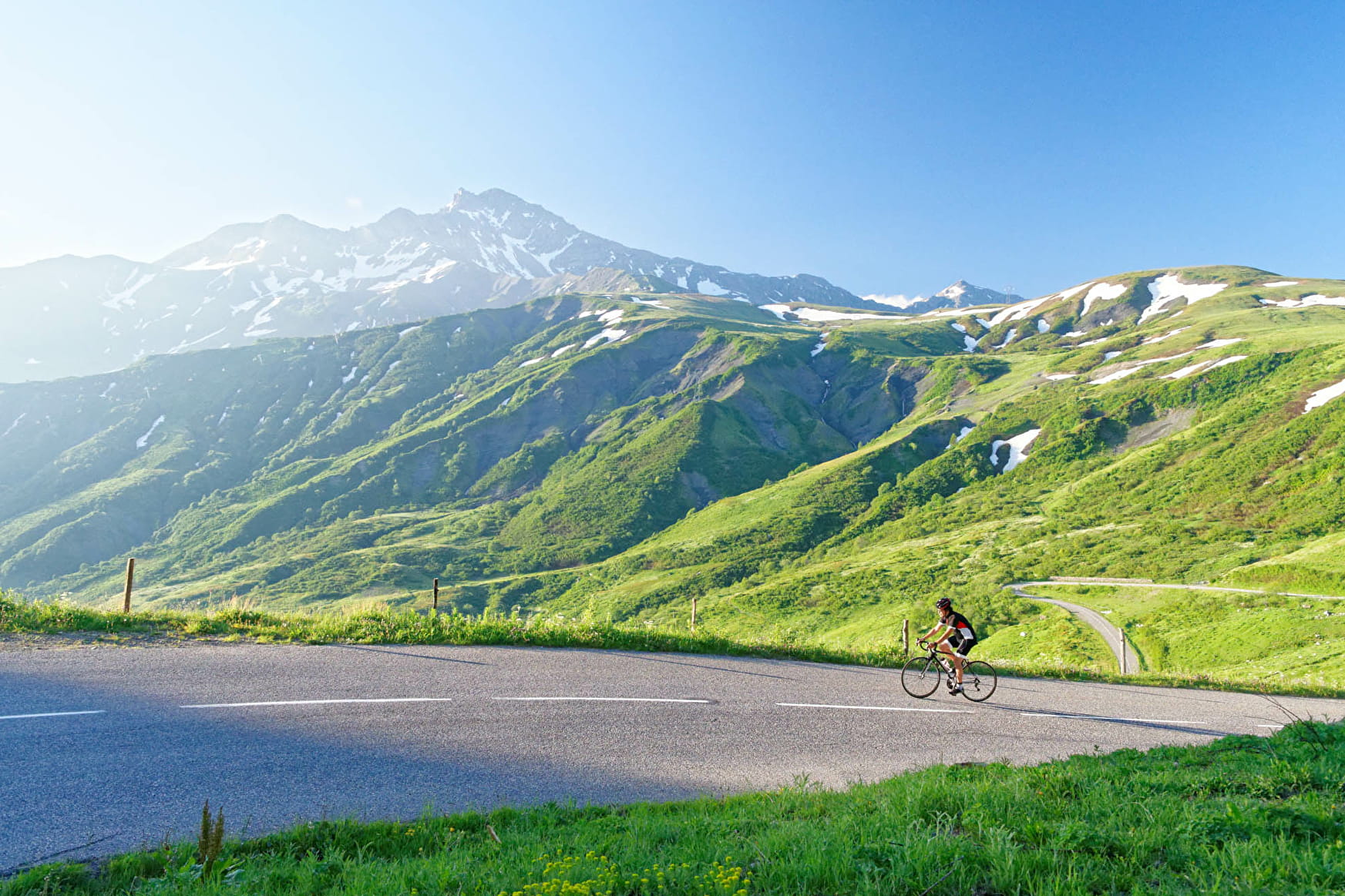 Cycliste sur la route du col de la Madeleine en Tarentaise — alpages et sommets enneigés en arrière-plan